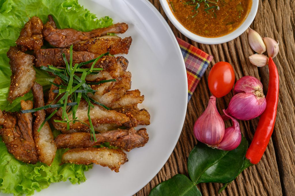 Pork neck grilled on a white plate wiht red onion, tomato, and c